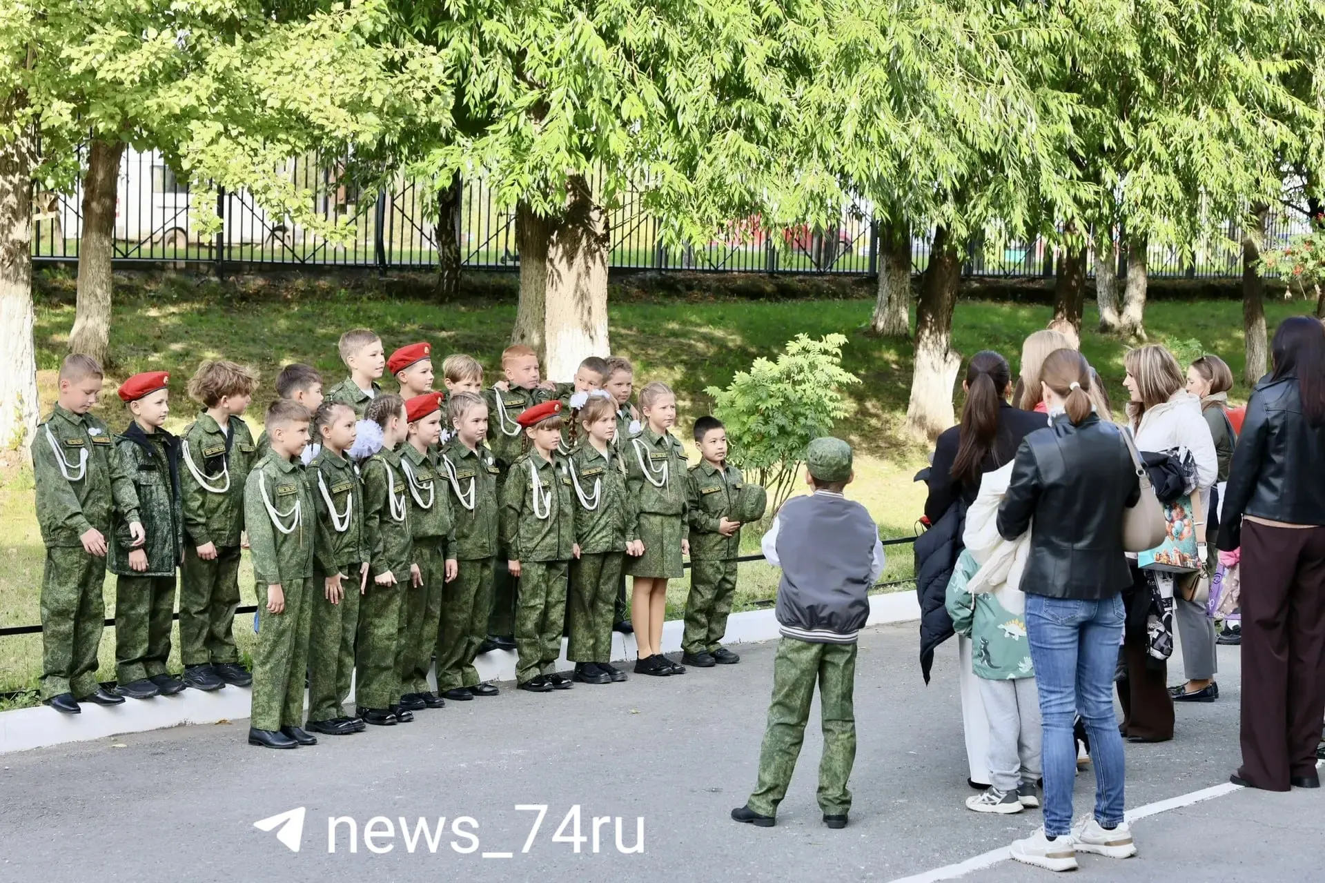 Ученики и родители собрались во дворе перед линейкой в спортзале; учителя поздравляют, кадры на память фиксируют торжественный момент.